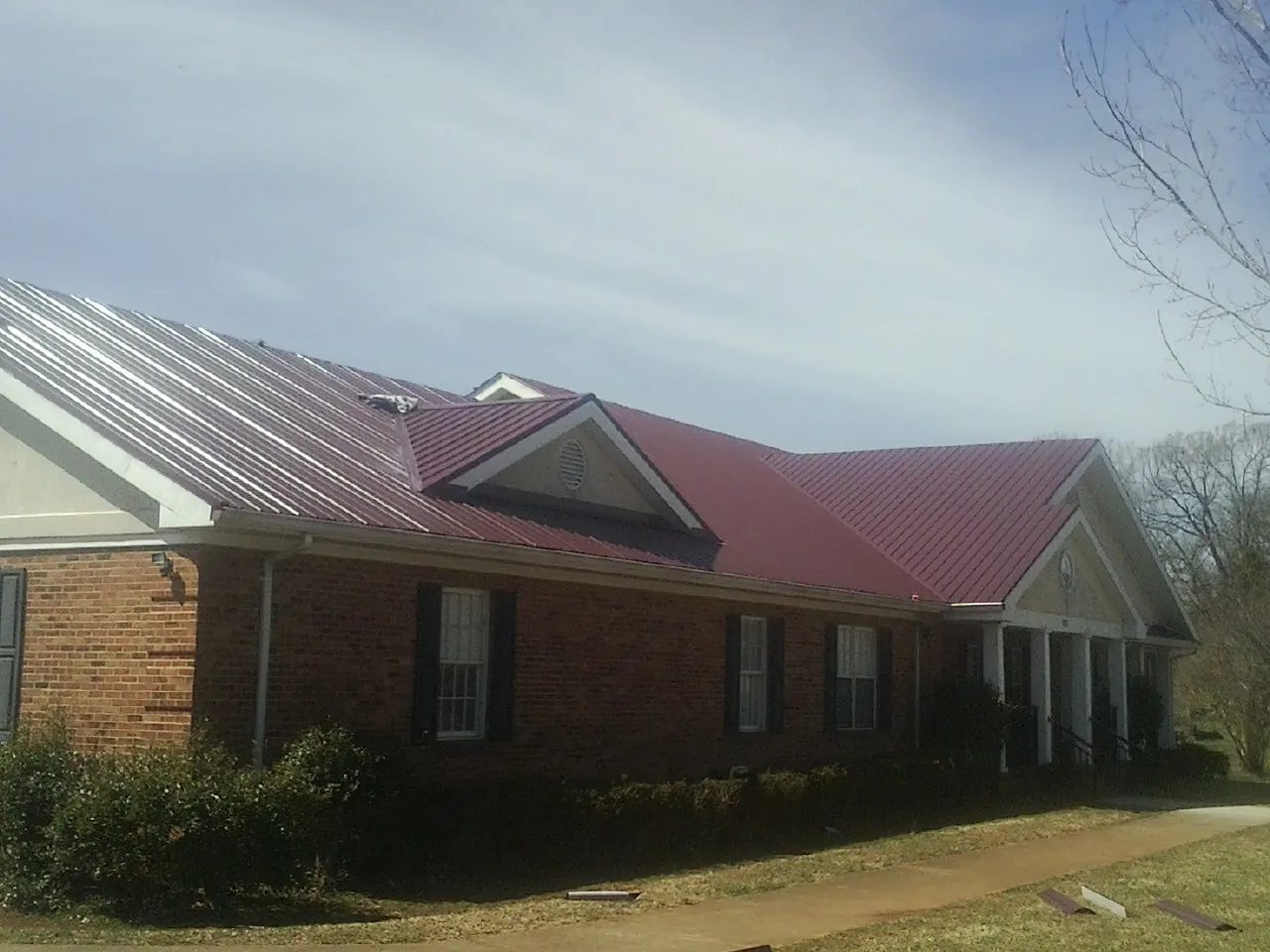 Red metal roof with gabled entries on a long brick building, from a Hail Damage Roof Repair job in Garrattsville