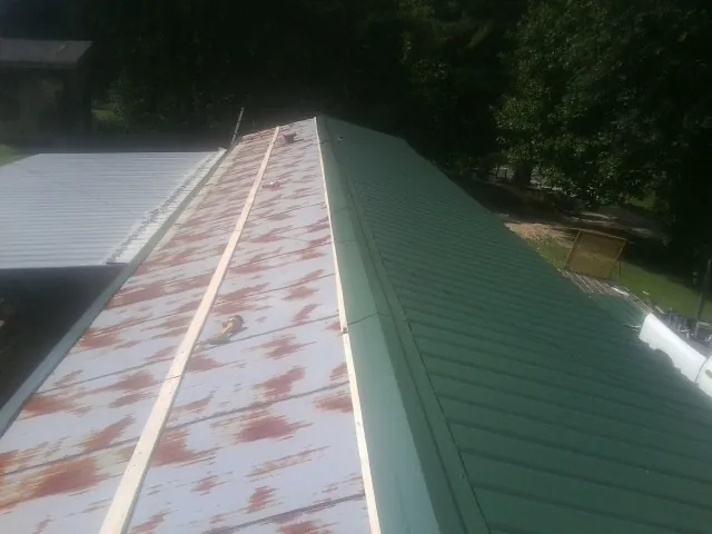 Old rusted panels beside newly installed green metal roofing — Wind Damage Roof Repair by Roofing Brothers in Garrattsville