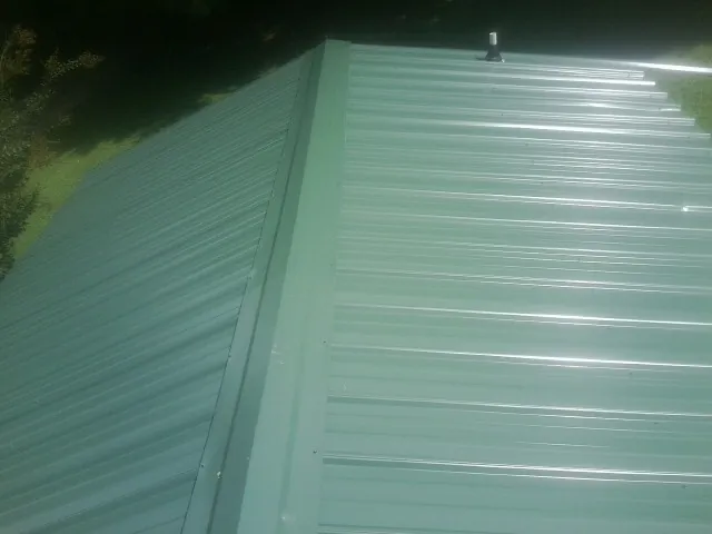 New green metal panels meeting at the ridge of a roof — Flat Roof Repair work by our crew in Garrattsville
