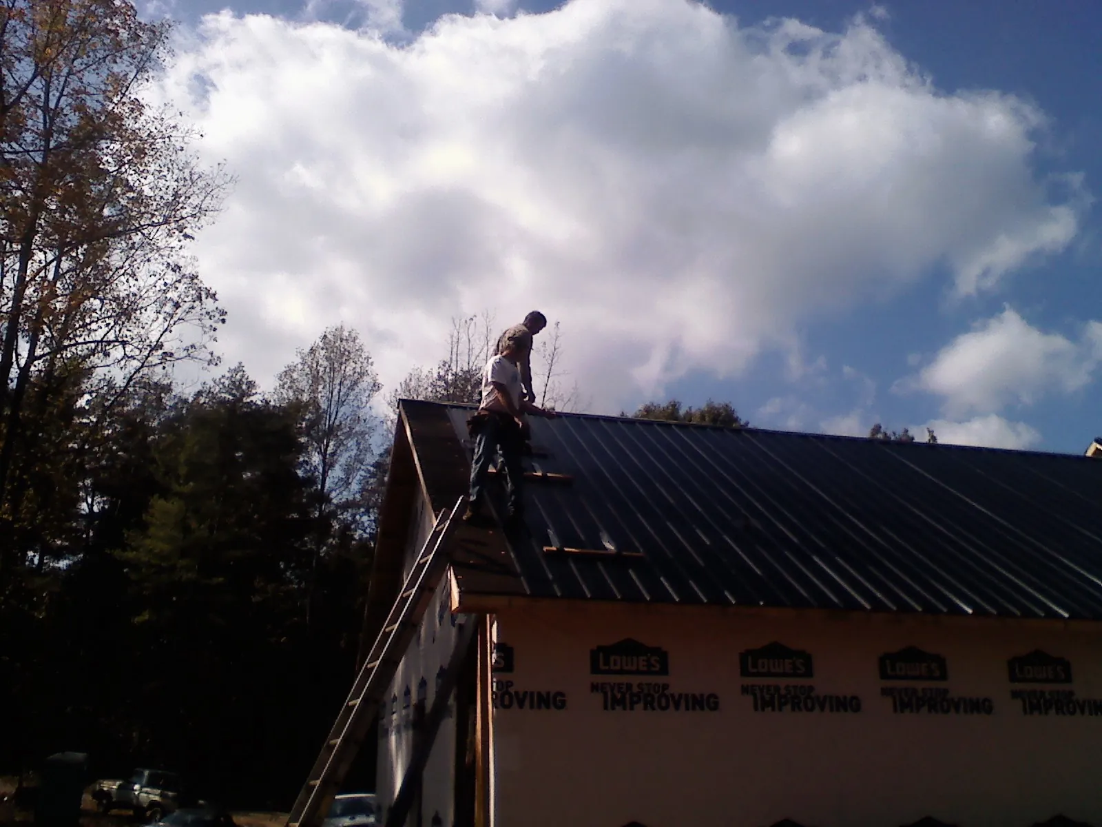 Roofer fastening dark metal panels high against a cloudy sky, from a Roof Inspection job in Garrattsville