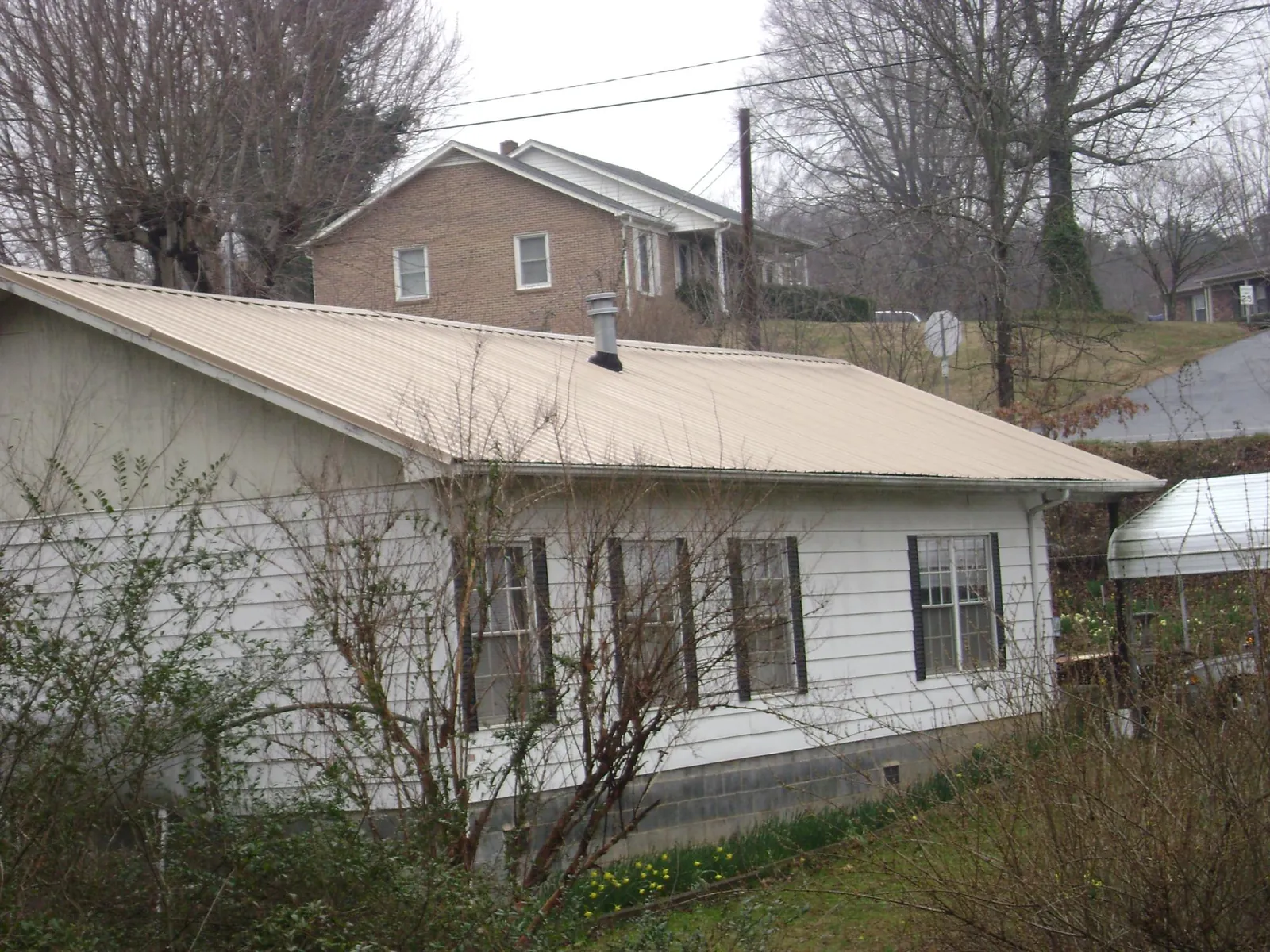 Tan metal roof on a white sided house set into a hillside — Commercial Roofing by Roofing Brothers in Garrattsville