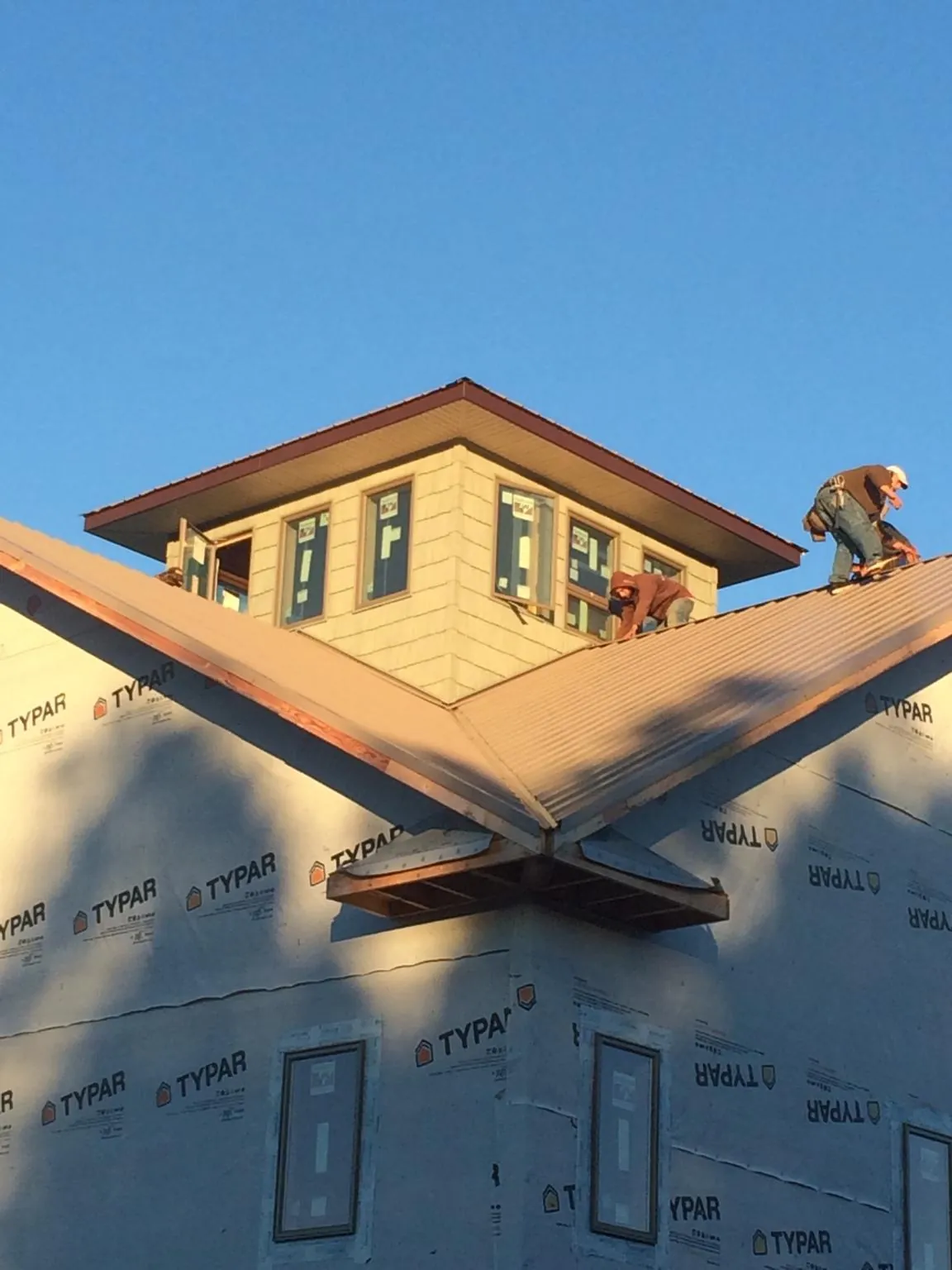 Roofers working around a rooftop cupola on a new metal roof at sunset — Roof Waterproofing in Garrattsville by Roofing Brothers